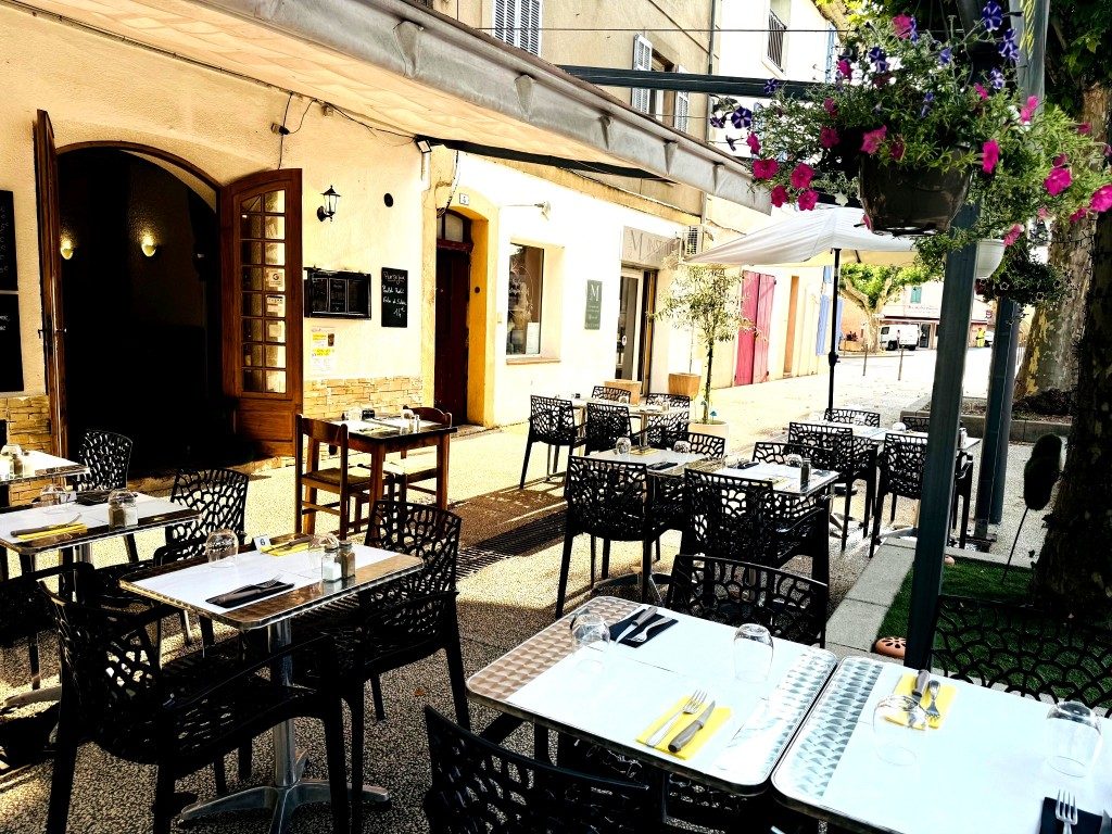 La terrasse fleurie : tables, chaises et suspensions de fleurs sous la façade ocre